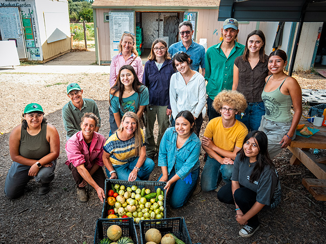 Community farm group smiling with crates of tomatoes, melons, and squash. UC Davis Department of Plant Sciences